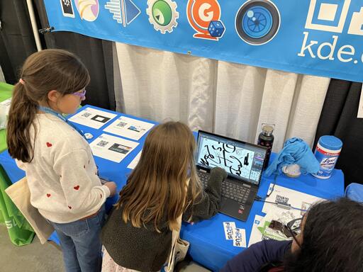 Two children, maybe 7 or 8, try out Krita, the full-featured painting program for artists, on a laptop at KDE's booth.