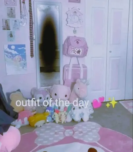a mirror on the wall of a pink room with plushies around it. the reflection in a sinister shadow, with text below it reading: "outfit of the day *two hearts emoji* *stars emoji*" 