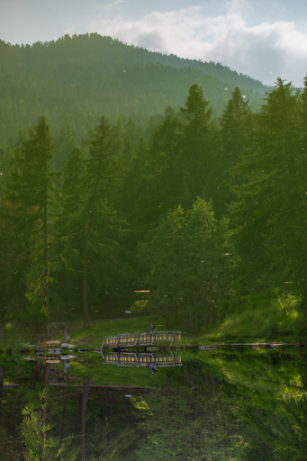 a flipped photo: mostly the reflection in a little lake of a moun tain with green trees; also a pedestrian bridge along the waterfront, with two people barely visible. 