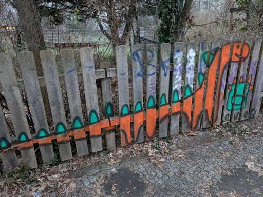 Orange dinosaur sprayed on wood fence, the dino has long neck and tail and green spikes on the back