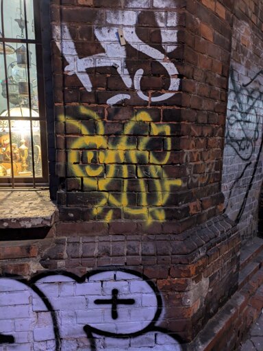 Yellow bee drawn with a spray can on brick wall. Next to a window and graffiti tags